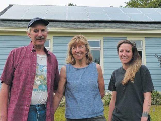 A family stands outside. Behind them the roof of their home holds a group of solar panels.