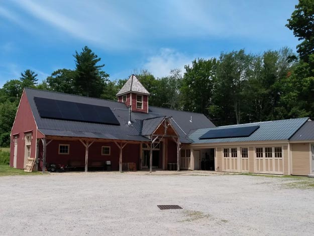 A barn and stables with two sets of solar panels on the roof.
