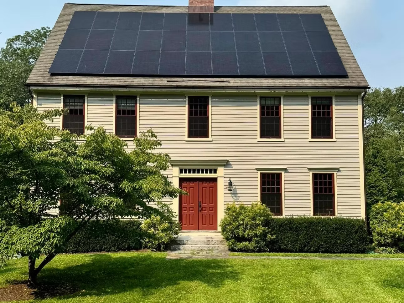 Solar panels rest atop the roof of a beige colonial style home.