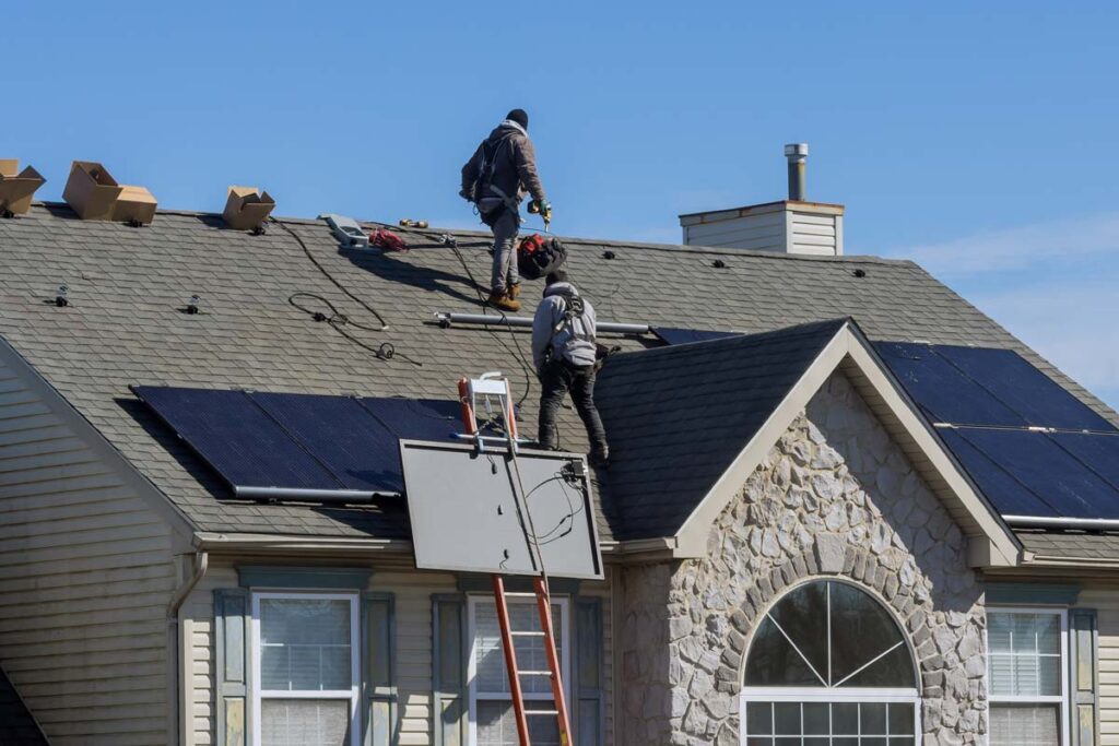 A solar panel installation team climbs the roof of a house.